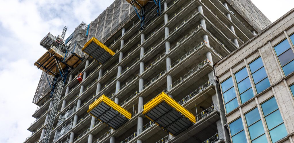 Concrete tower in progress with yellow cantilever loading decks and scaffolding. Strong modular geometry, low angle city view, modern development with no people. SSUCv3H4sIAAAAAAAAA41PQY6DMAz8i88gkdBIha9UewiJoVaBVInZaoXy93Uo1V43pxlPPDPegTz0oNWAnTZNbb3VtVJjU3dOm9qMyo/mch2d8lCBt4zQq/bSGNM22ui2uzbyKhhsIgf9DjTPW+JomcIKvSgRV4/xgOiJQyQ7C8sVJLa8JUyyJsyJ9yTqwT9+t73MpaCEp20oIFf/nH1VYCdc3U/xz6XIjPaIu4n0eDHG5cwOfC8VC3xGcrROZyc5JSxvvAYuu0cCB/cgfy6/z7iTTGPJgu05B+vRn/I2LMT8oRG/CV9/v3POv0FU4M+EAQAA